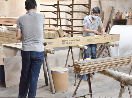 A worker handling wooden components on a large machine, ensuring precision in the woodworking process.