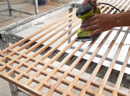 A worker is using power tools to finely process wooden pieces, demonstrating skilled craftsmanship.