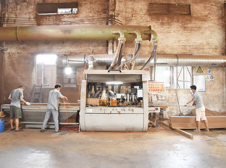 Workers operating machinery with stacked materials and equipment in a factory workshop.