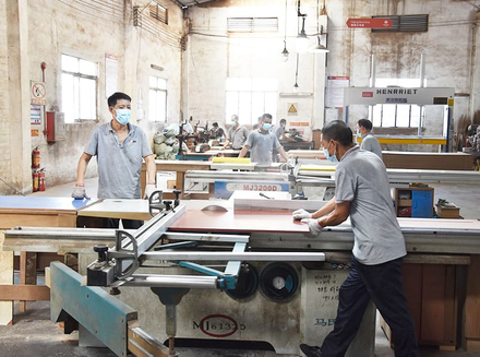 A worker operating a large machine with wooden panels in a factory workshop.
