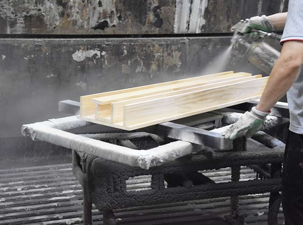 A worker is meticulously spraying paint on wooden pieces, ensuring an even surface.